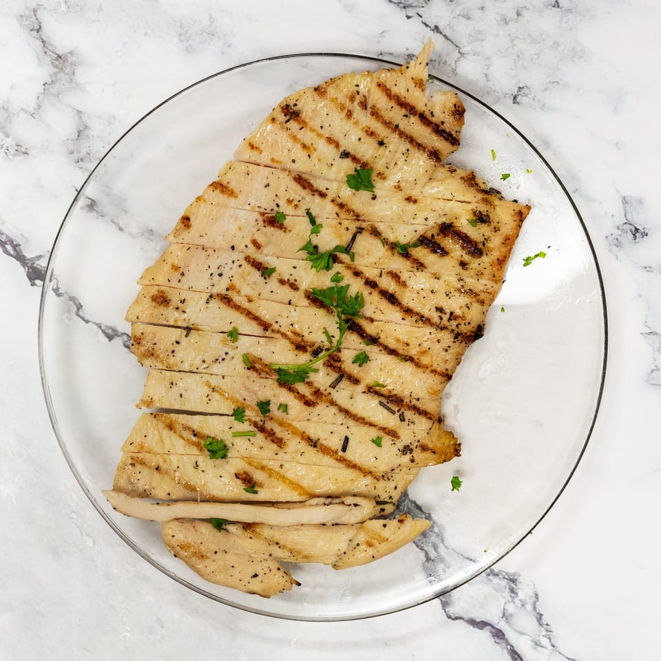 Grilled chicken breast, sliced and garnished with parsley, on a clear plate.