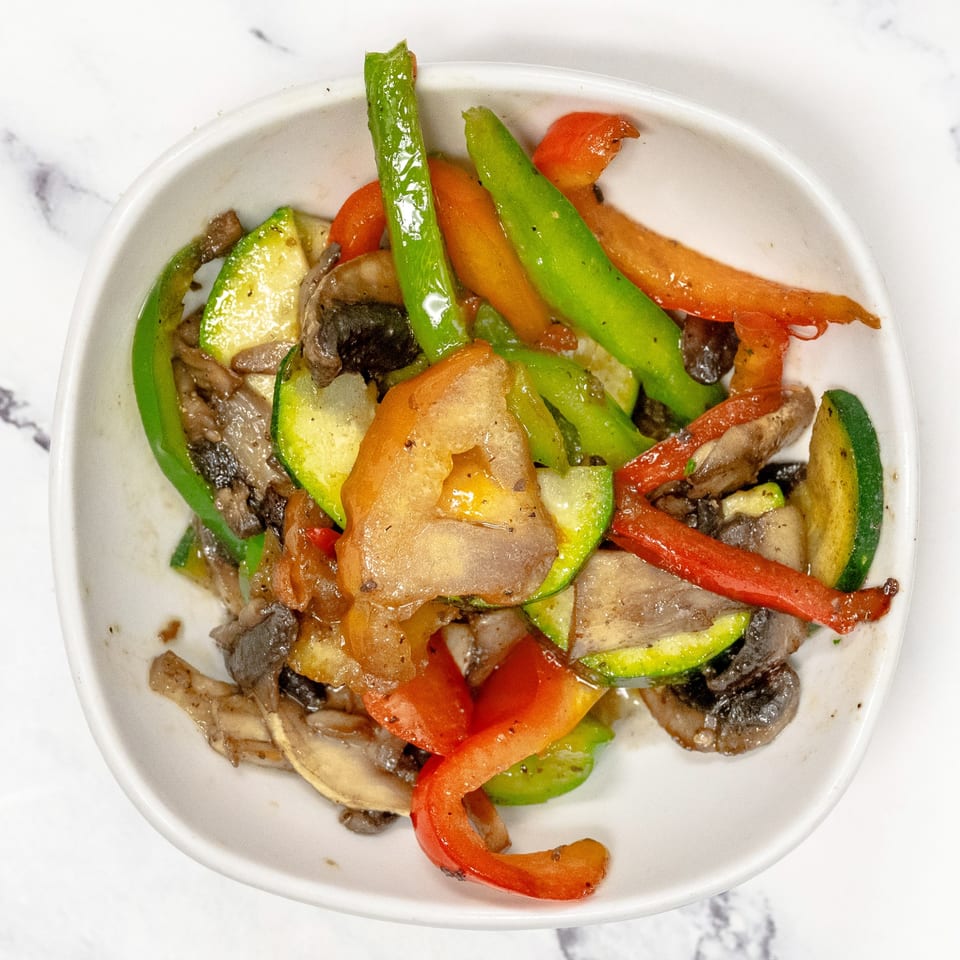 A white bowl filled with sautéed zucchini, mushrooms, red bell peppers, and green beans.