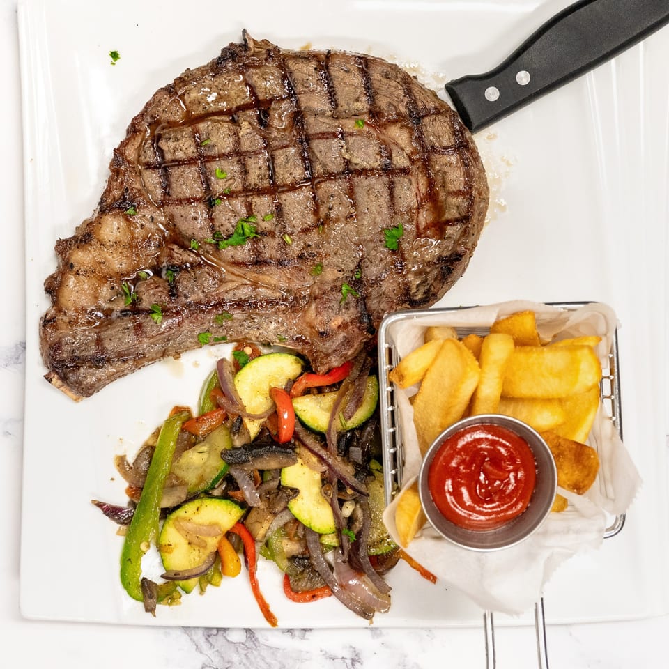 Grilled steak with sautéed vegetables, a side of french fries, and ketchup on a white plate.