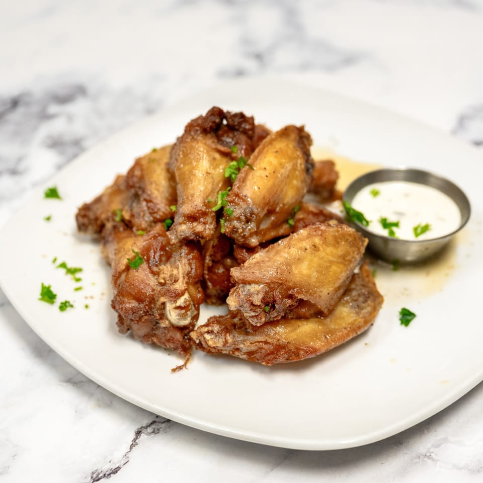 Crispy Frank & Sons chicken wings with parsley garnish and a side of ranch dressing on a white plate.