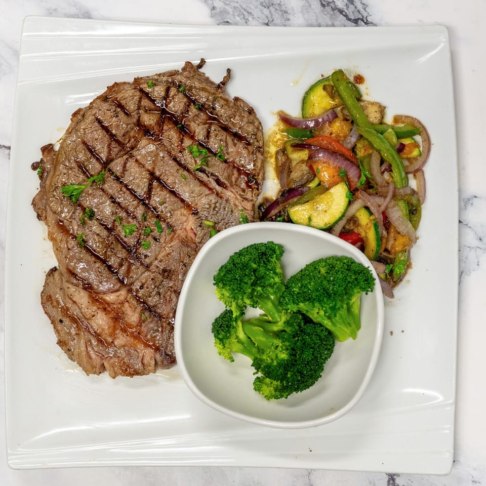 Grilled steak with char marks, sautéed vegetables, and a side of steamed broccoli on a white plate.