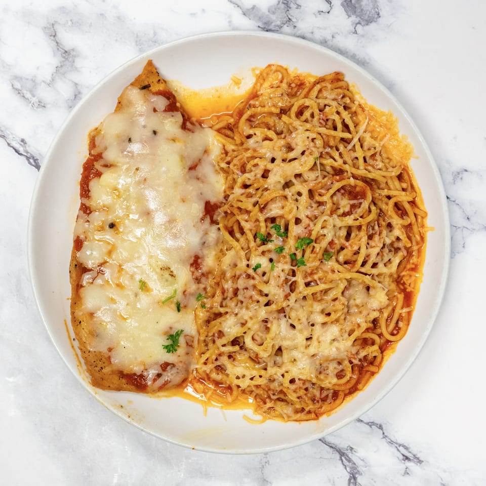 Chicken parmesan with melted cheese and a side of spaghetti with meat sauce and parsley.