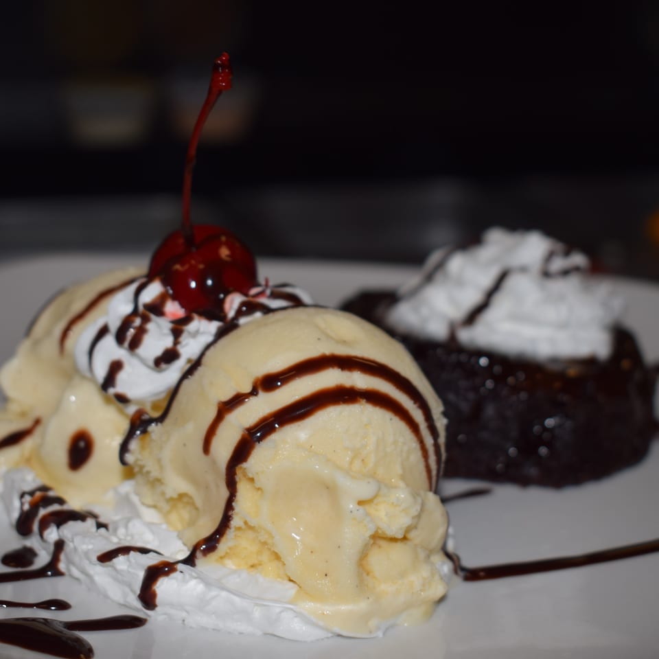 Vanilla ice cream with chocolate syrup and a cherry next to a chocolate lava cake.
