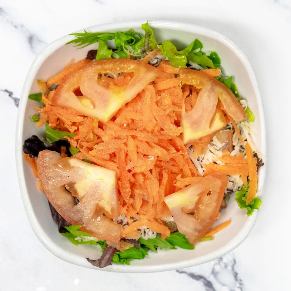A fresh garden salad with lettuce, shredded carrots, and sliced tomatoes in a white bowl.