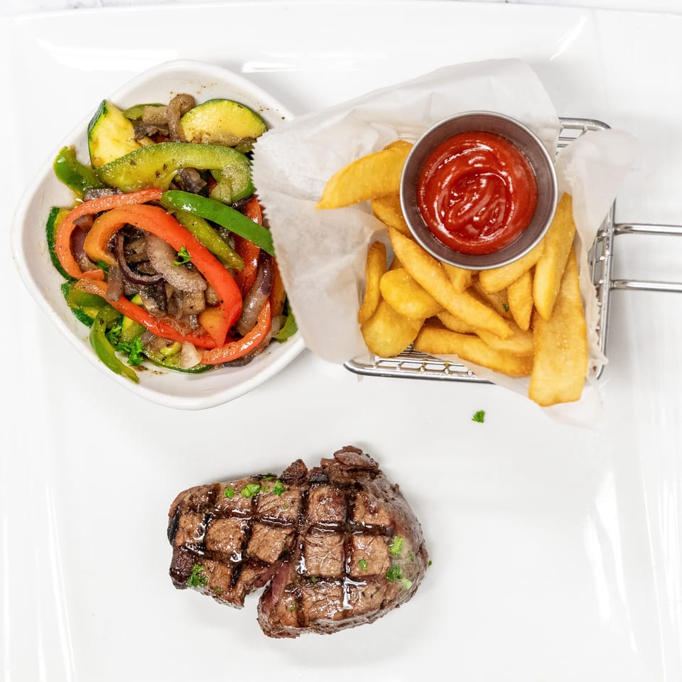 Grilled steak with sautéed vegetables and a side of french fries with ketchup.